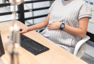 a pregnant woman touching her belly while using the computer
