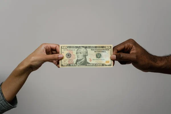 two hands holding on each end of a ten dollar bill