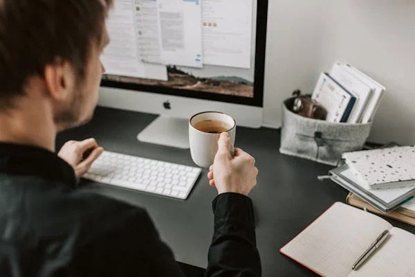 a man holding a cup of coffee in front of his computer