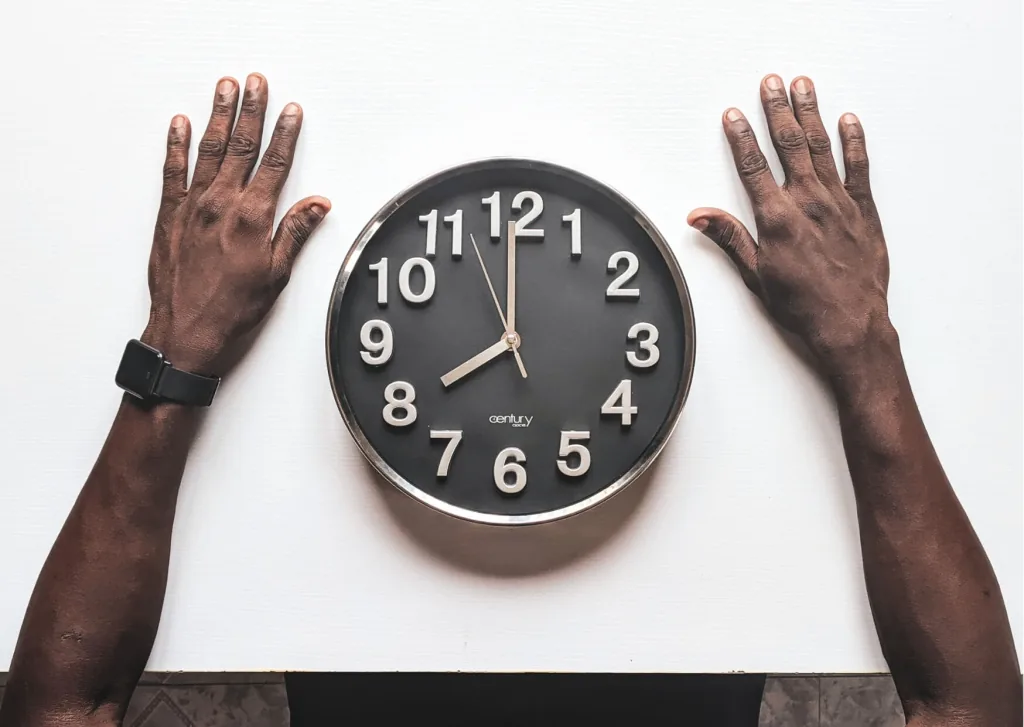Worker's hands framing a wall clock, illustrating time clock rounding of work hours
